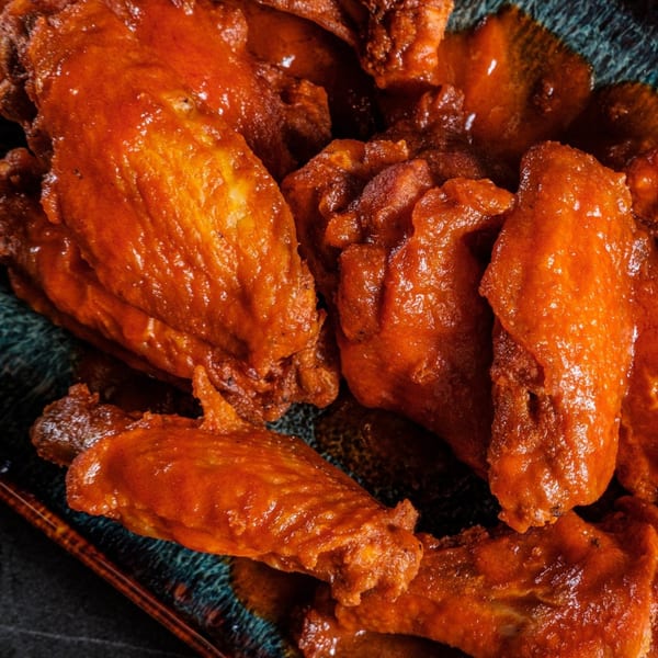 Close-up of several glossy, orange-red chicken wings on a dark, textured plate.