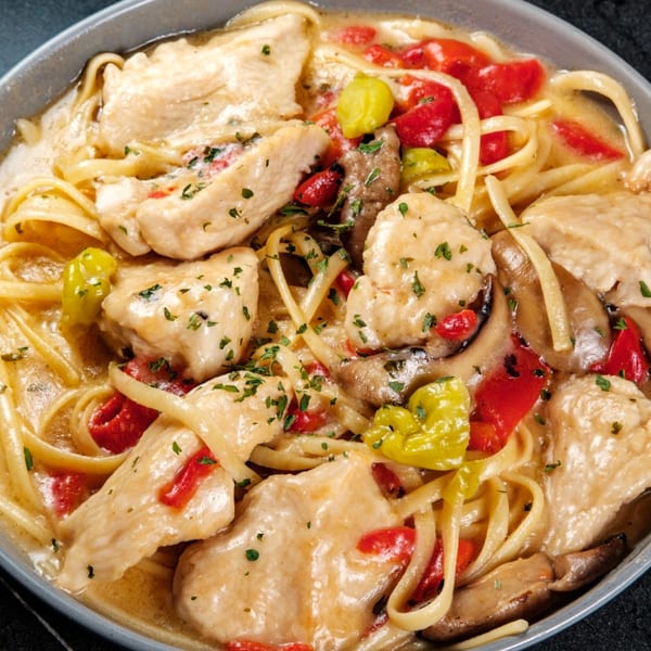 Creamy chicken linguine with red and yellow peppers, mushrooms, and parsley in a gray bowl.