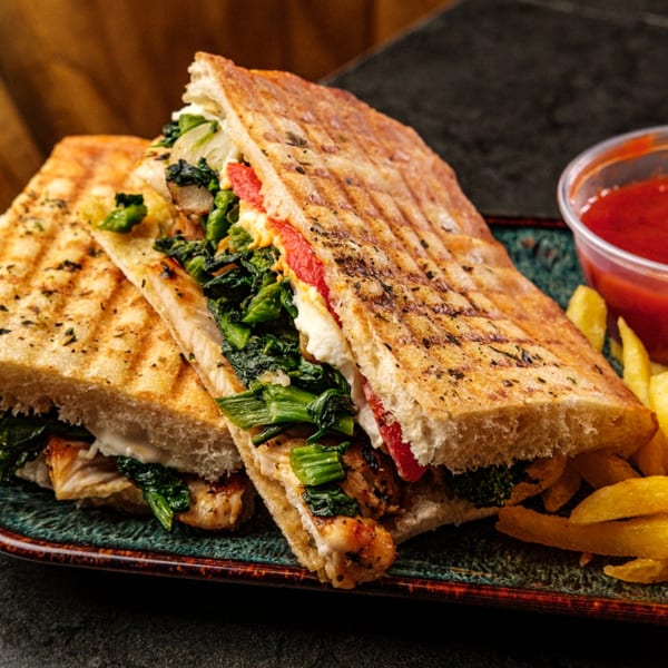 Grilled panini sandwich with chicken, spinach, and red peppers, served with fries and ketchup.