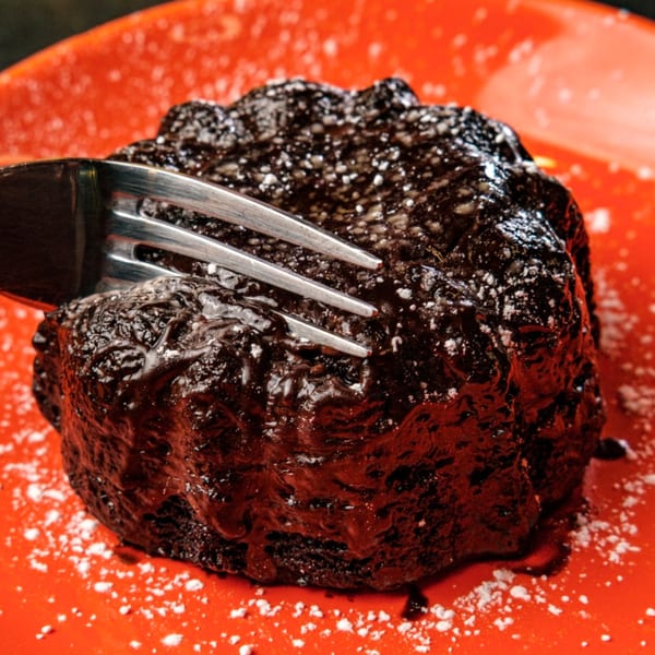 A fork piercing a rich, dark chocolate lava cake dusted with powdered sugar on a red plate.