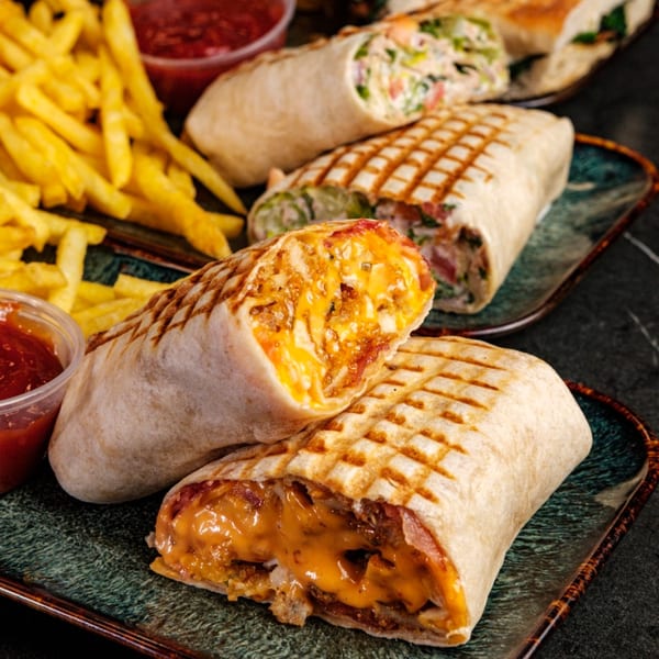 Three grilled wraps, one cut open to show melted cheese and filling, with fries and ketchup.