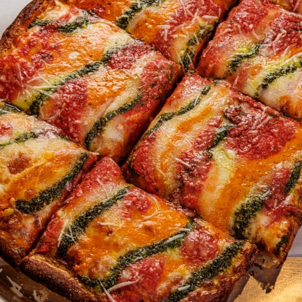 Close-up of a square Pizza One pizza, cut into slices, with red sauce, pesto, and cheese.
