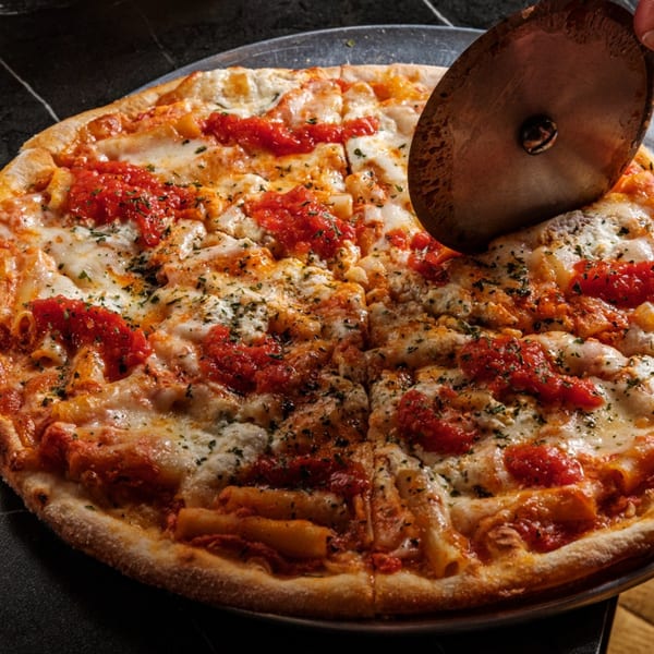A pizza with tomato sauce, melted cheese, and pasta, being cut with a pizza cutter.