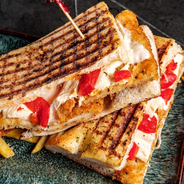 Grilled panini sandwiches with melted cheese, red peppers, and a side of fries on a dark plate.