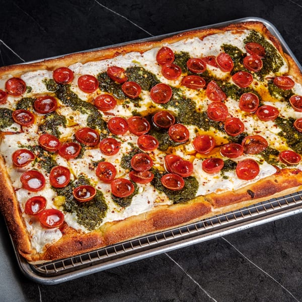 A rectangular Pizza One pizza with white cheese, green pesto, and red cherry tomatoes on a metal tray.